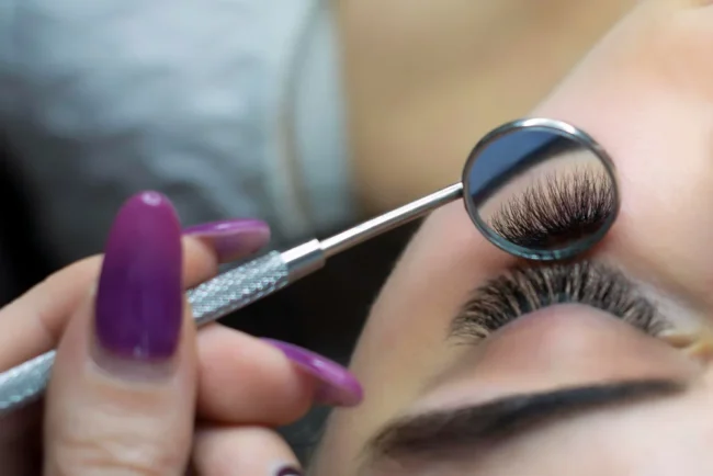 Blog Bild zum Beitrag wie lange hält Wimpernverlängerung. Eine Wimpernverlängerung wird mit einem Zahnarztspiegel von unten gezeigt.